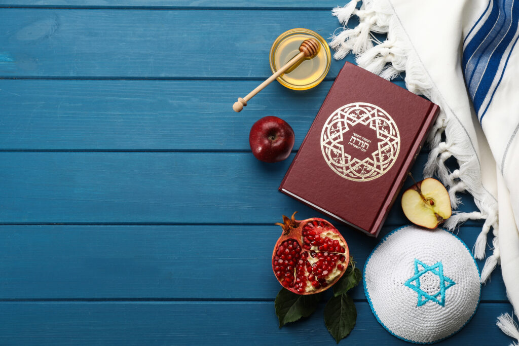 Flat lay composition with Rosh Hashanah holiday attributes on blue wooden table. Torah book with text in hebrew