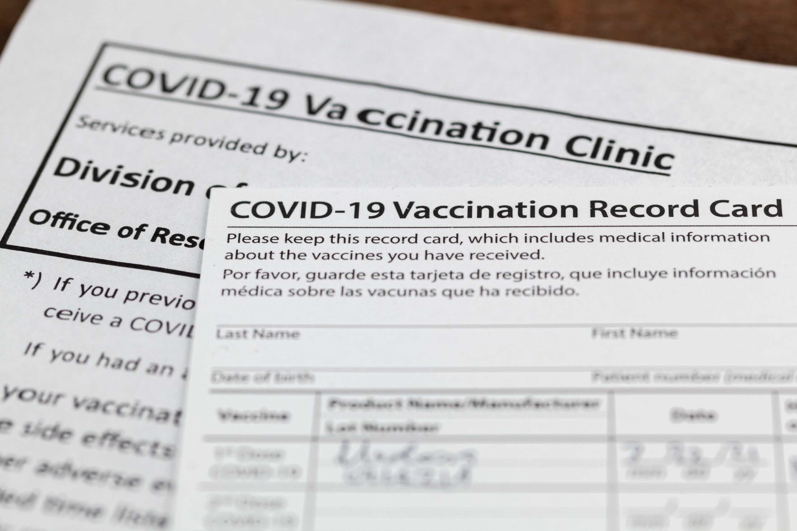 Close up isolated image of a COVID 19 vaccination record card on a wooden desk. The card details the date, type and the dose number of administred vaccine and given to every person for record.