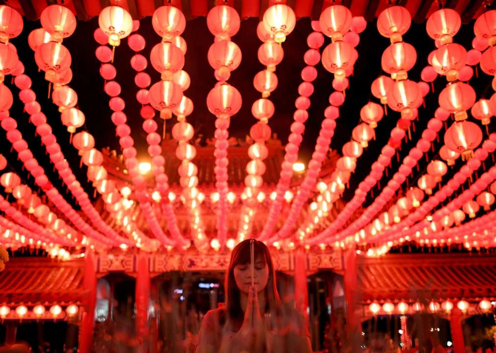 A female holds her hands together in prayer under red string lights
