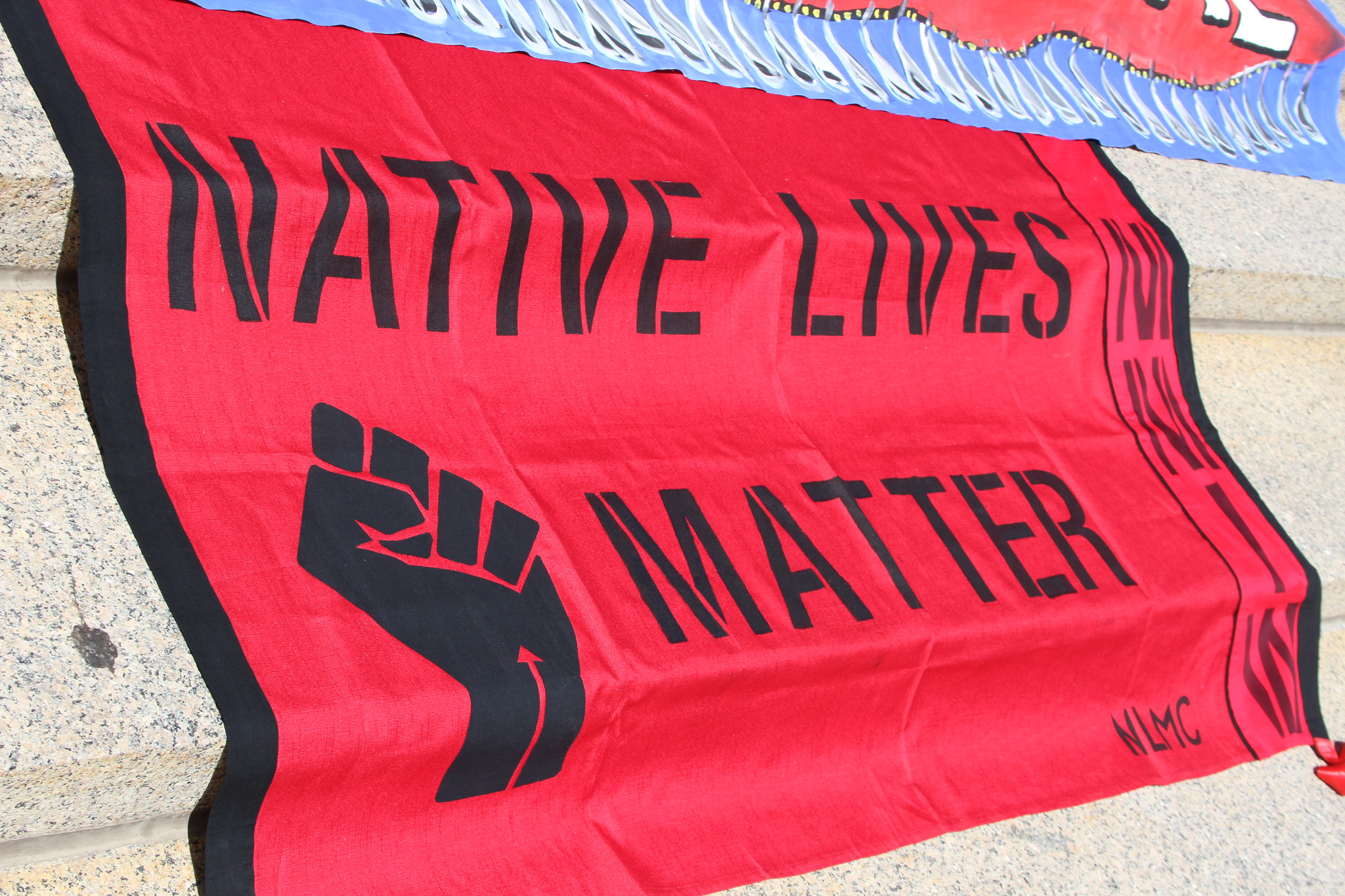 A large red banner reading "Native Lives Matter" with a fist drapes over stairs