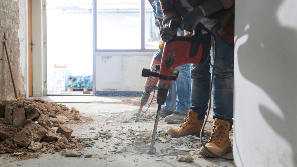 Two large powertools jackhammer into concrete on a home reno construction site