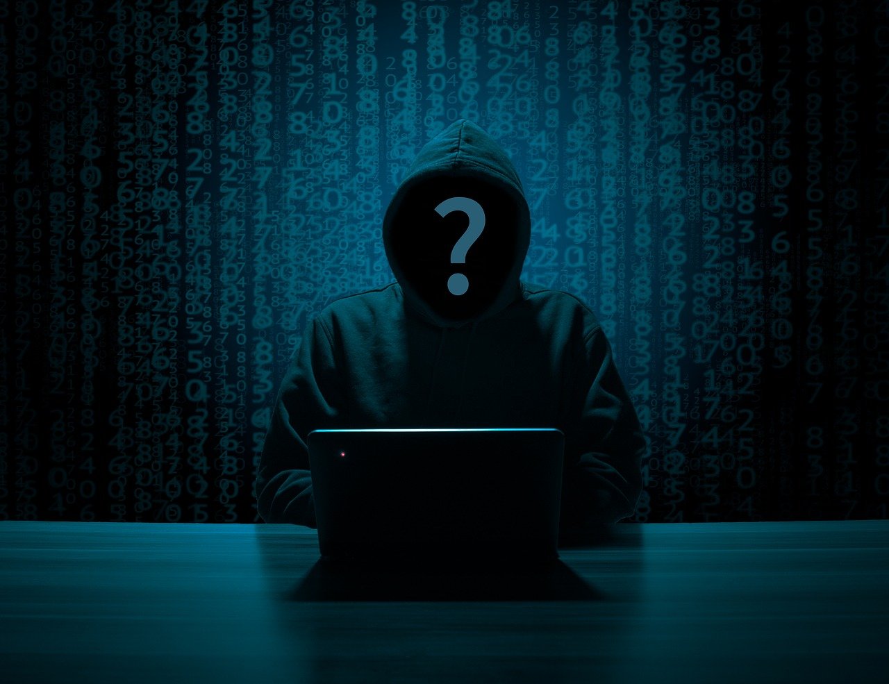 A shadowy figure in a hoodie, their face replaced with a question mark, sits at a laptop. Blue computer code is the background behind them. The image portrays what appears to be a hacker or cybercriminal