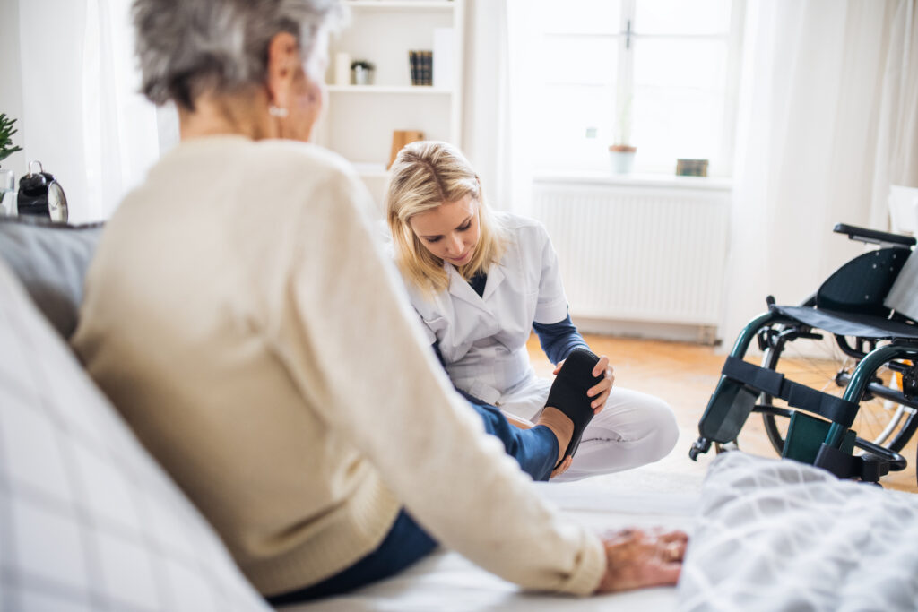 A young in-home care provider putting on slippers on a senior woman at home.