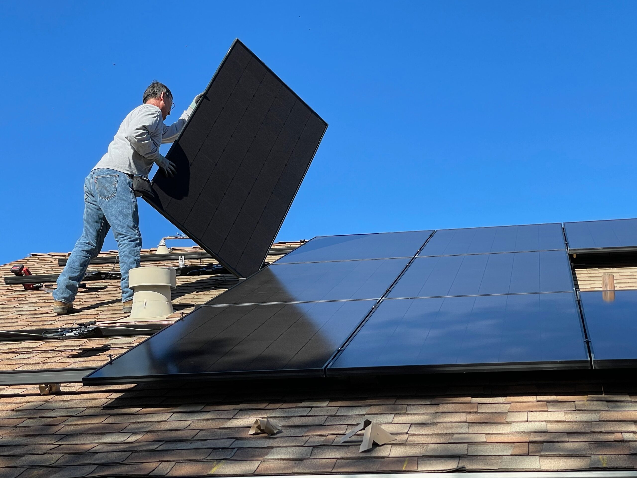 A worker installs solar panels on the roof of a house