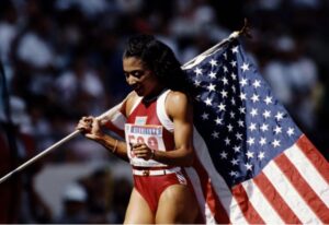 A black female olympian holds the American flag as she celebrates