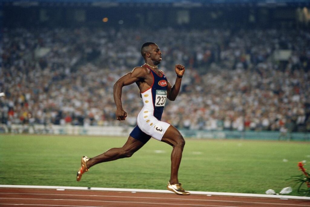 A Black male professional track runner, Frederic Haslin, races full tilt down the track