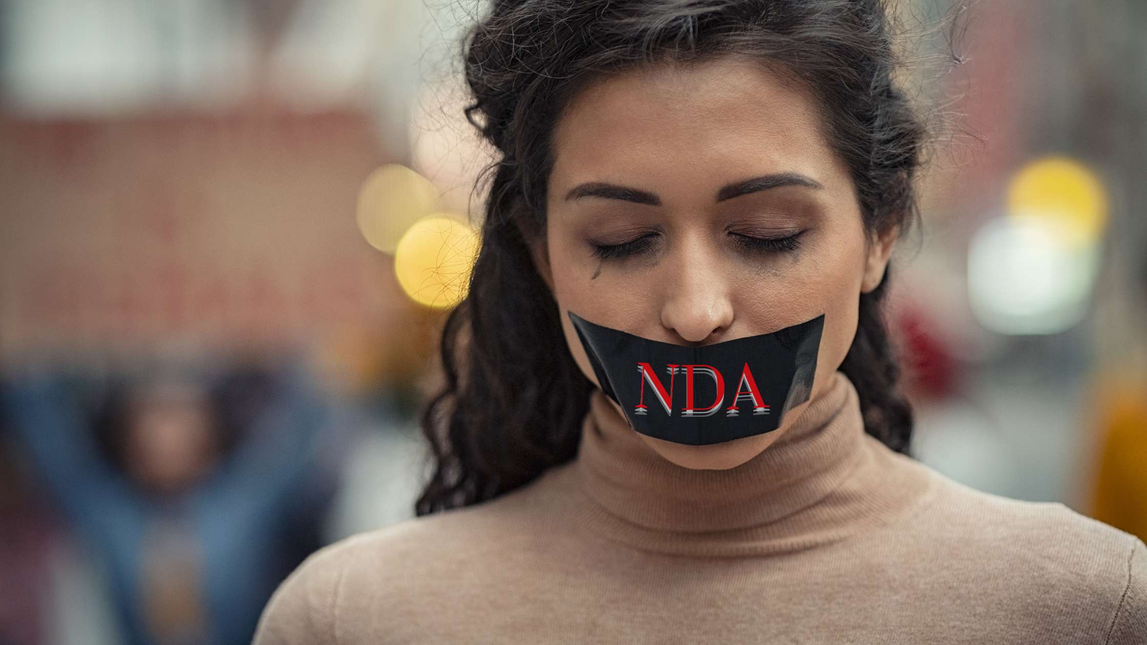 A female with tape with the word NDA covering her mouth looks down