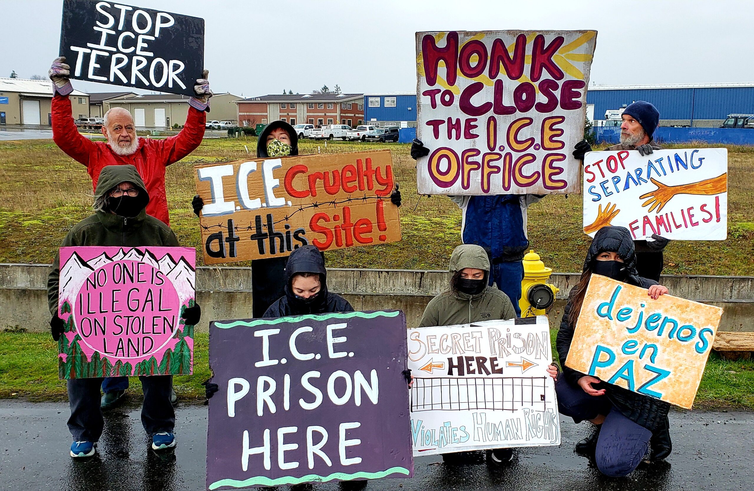 individuals protesting the ICE detainment facility hold protest signs