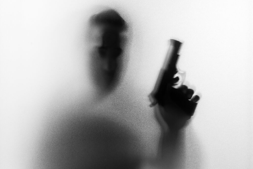 Shadow of horror man killer with a gun in his hand.Dangerous man behind the frosted glass.Mystery man.Halloween background.Black and white picture.Blur picture