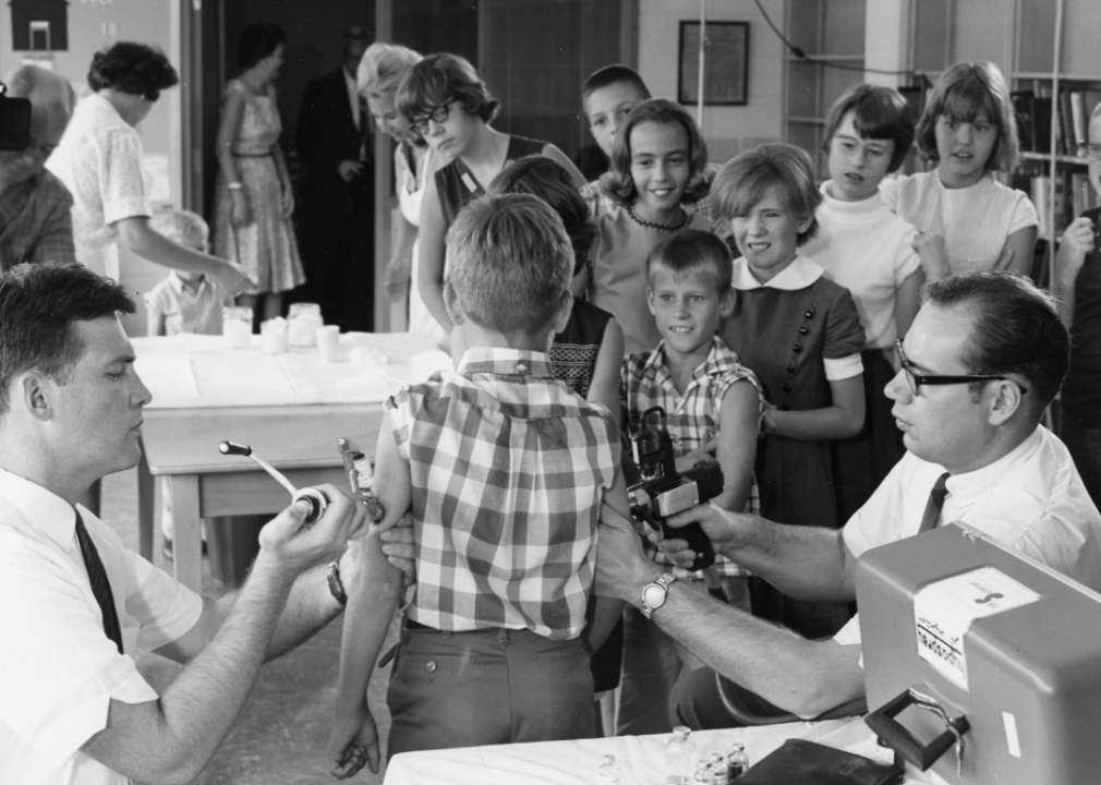 An old photo of two males administering vaccines to a young boy