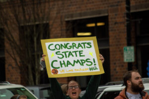 a woman holds up a sign that reads "Congrats State Champs"