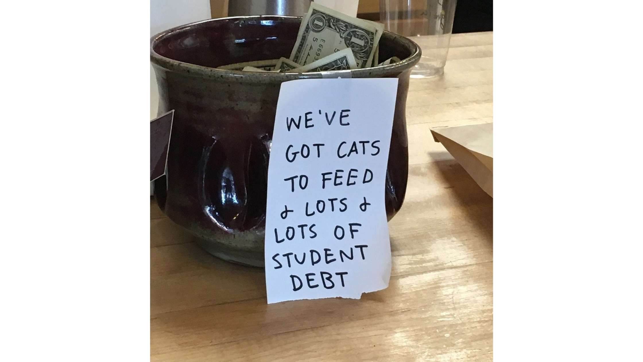 A tip jar at a coffee shop has a note telling customers they have cats to feed and lots of student debt.