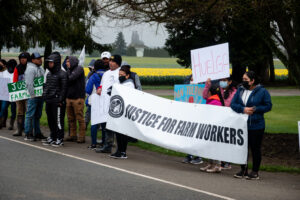 Skagit Valley farmworkers stand together with a large banner that reads "justice for farm workers"