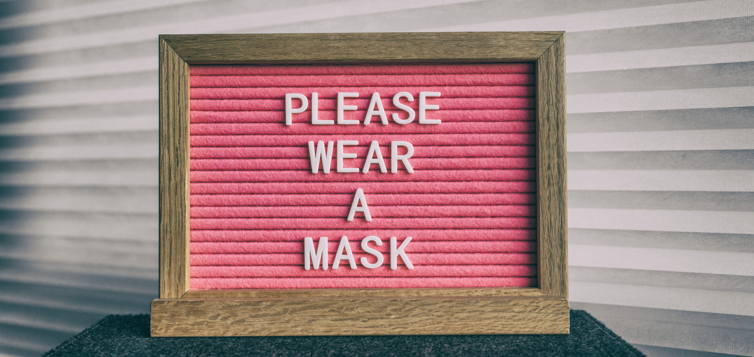 Please wear a mask pink sign at business store entrance message. Obligatory wearing of COVID-19 protection face cover.