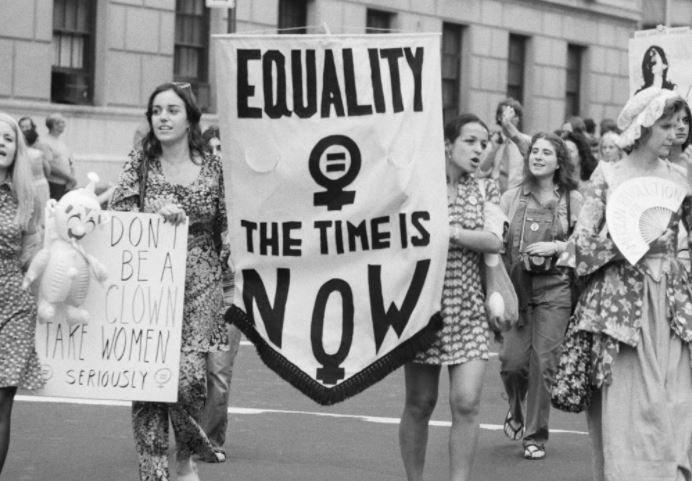 a black and white photo capturing a moment in women's history of of women marching, holding signs with messages demanding equality