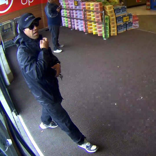 An adult male walking into a store wearing sunglasses, a hat and hoodie