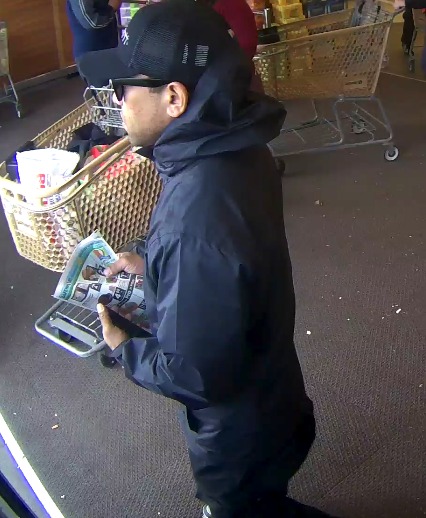 An adult male walking into a store wearing sunglasses, a hat and hoodie
