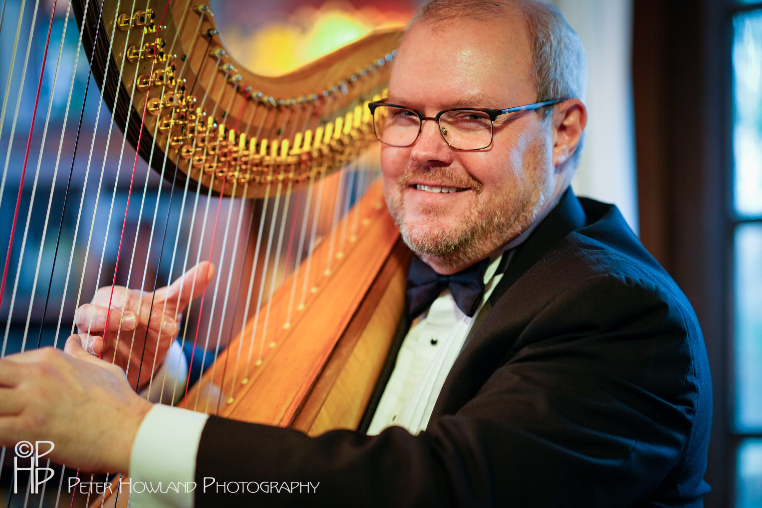 John Carringotn, a white middle aged man, plays the harp