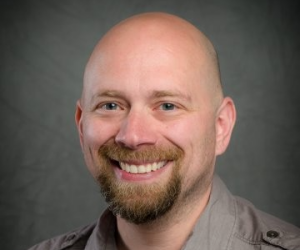 A headshot photo of Justin Greywolf, a middle age Caucasian male with a goatee and bald head