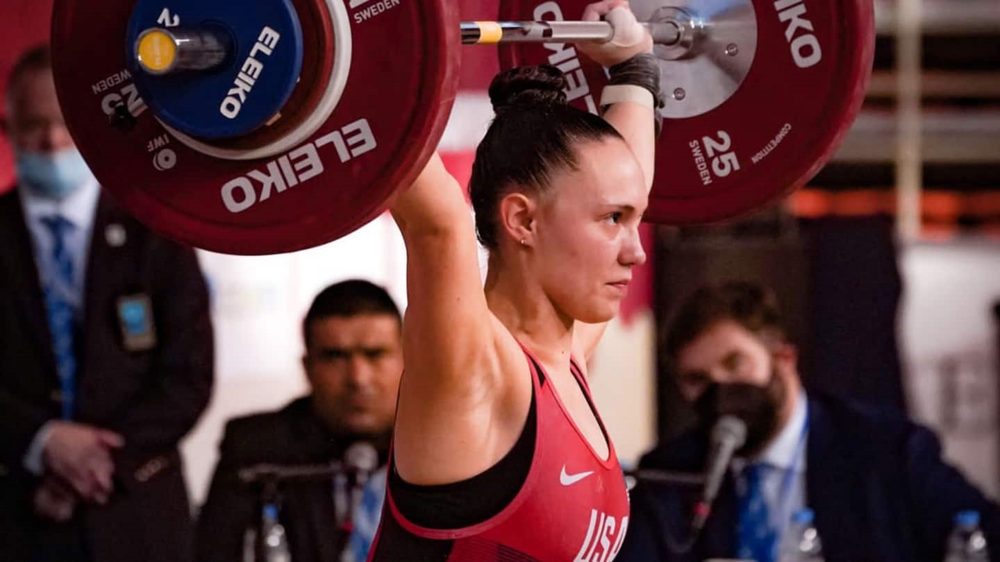 A female athlete, Meaghan Strey, focuses at she holds a large barbell above her head