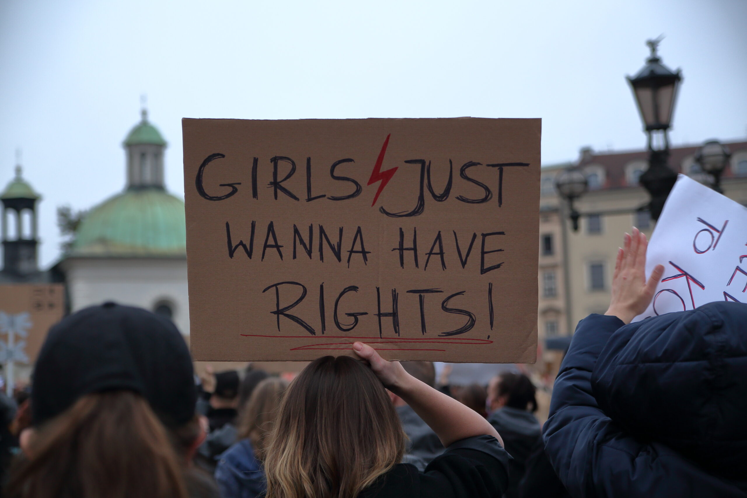 A cardboard protest sign is held up, the sign reads "girls just want to have rights"
