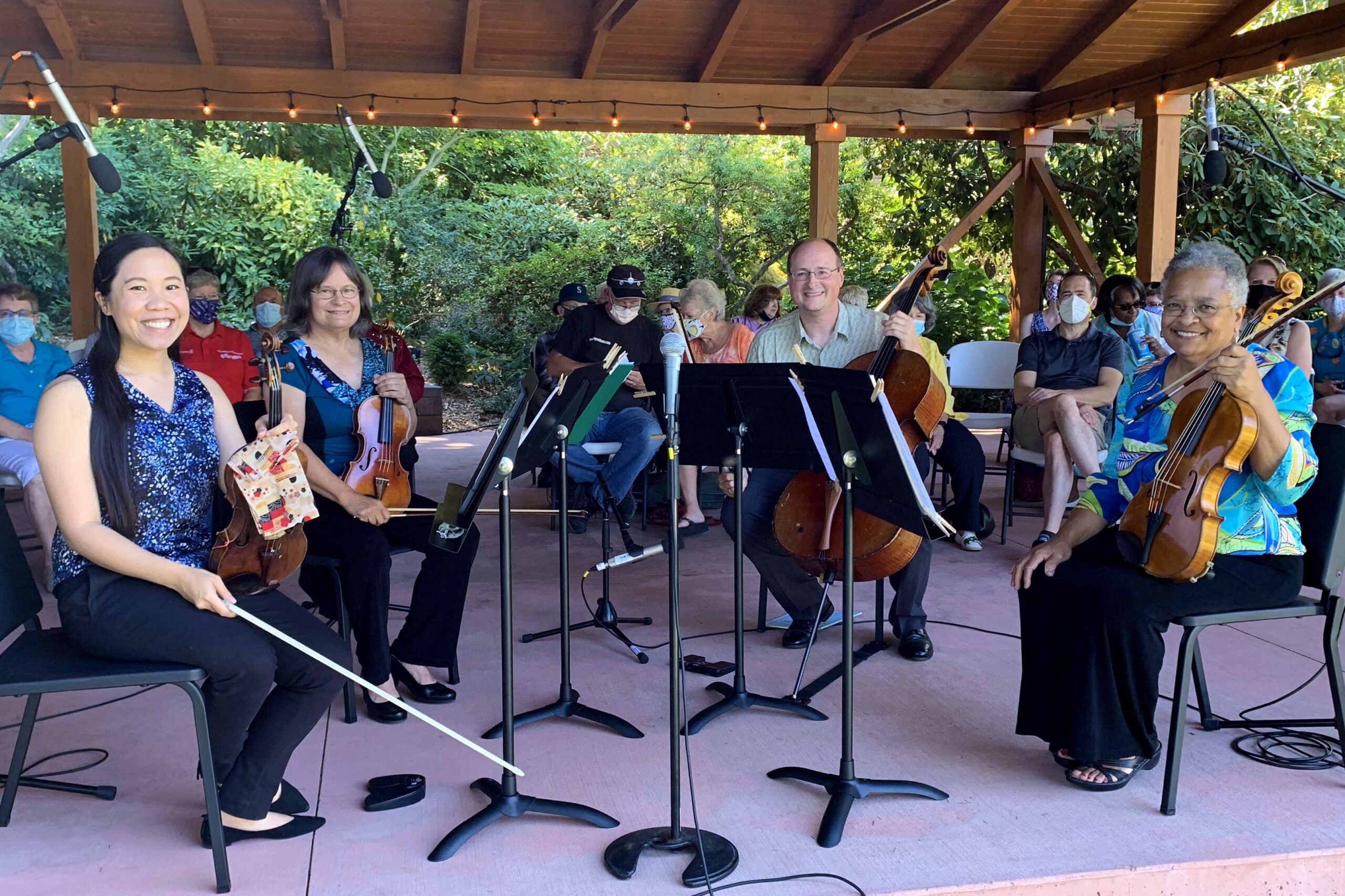 Musicians with classical instruments sit in a gazebo playing