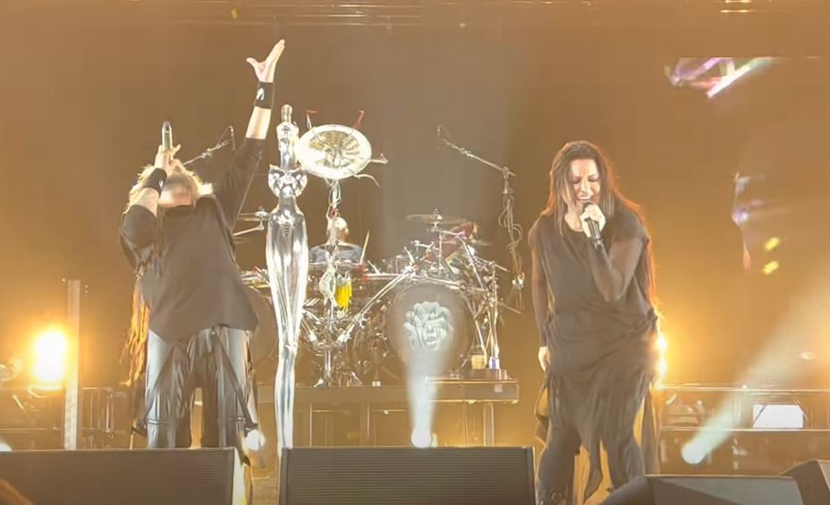 A male (L) and female (R) singer perform on a stage, the drummer playing in the background. The band is Korn and female is Amy Lee from Evanescence