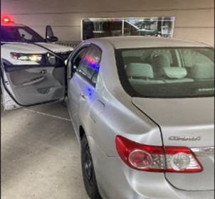a silver sedan is blocked in by a WSP SUV, at a drive thru bank ATM, facing the wrong way. The sedan's driver's door is open.