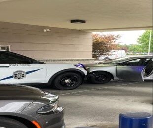 a silver sedan is blocked in by a WSP SUV, at a drive thru bank ATM, facing the wrong way. The sedan's driver's door is open.