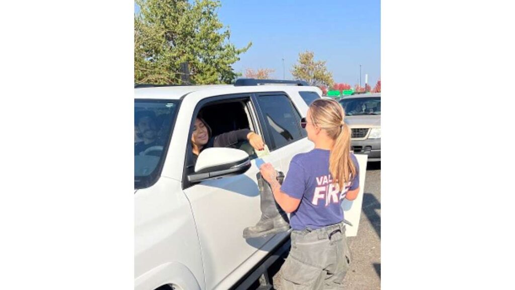 A female driver in a white SUV donates cash into a boot of a female firefighter