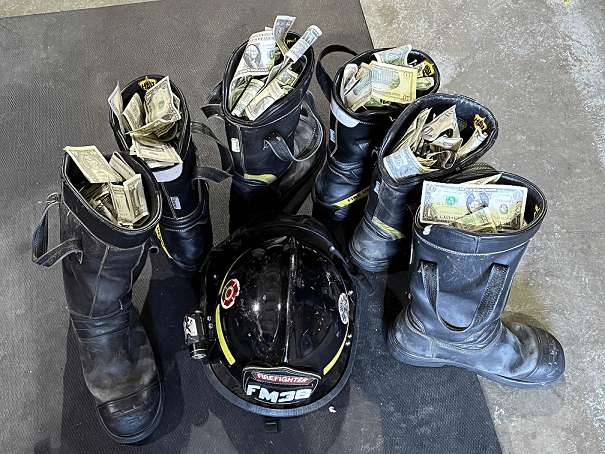 A firefighter helmet is surrounded by six firefighter boots filled with cash