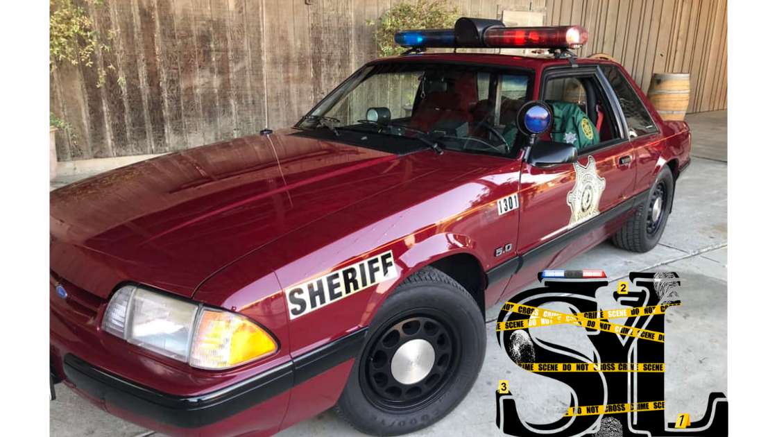 A red sport car with blue and red lights on top and a Sheriff's logo on the door