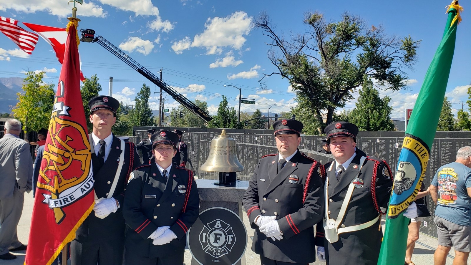 Four members of the VRFA honr guard stand in a line flanking the IAFF memorial bell. The individual on either end holds a flag, the left VRFA the right WA state.